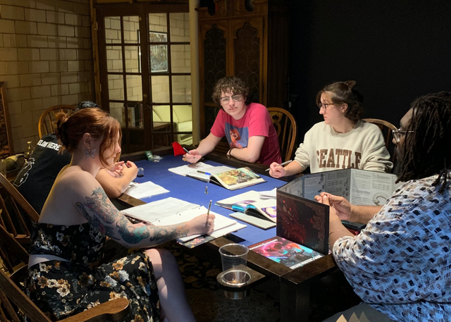 Four players and their game master sit at gaming table in small private room with gentle lighting focused on the dungeons and dragons books