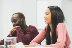 Young Black man and woman sit at a large table with books and drinks